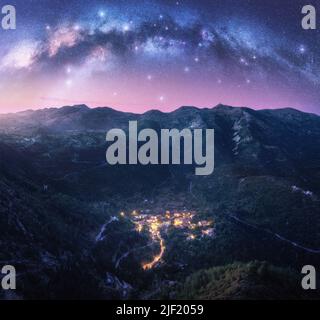 Arco Via Lattea e villaggio sulla montagna di notte in estate Foto Stock