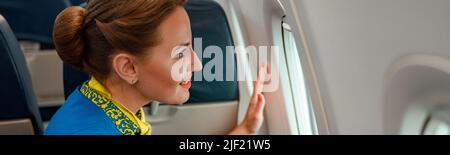 Donna gioiosa stewardess guardando fuori la finestra in aereo Foto Stock