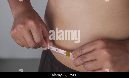 Concetto di misurazione. L'uomo misura una misura della linea della cintura con il nastro della vita egli stesso. Foto Stock