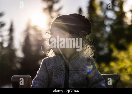 Primo piano ritratto naturale retroilluminato di un ragazzo caucasico di due anni che guarda a fianco nel bosco. Il sole brillante dona un'atmosfera creativa all'obiettivo. Foto Stock