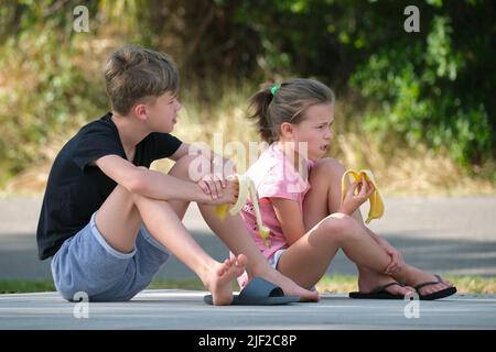 Giovane ragazzo bello e bella ragazza mangiare gustoso banana matura snacking all'aperto il giorno d'estate. Foto Stock