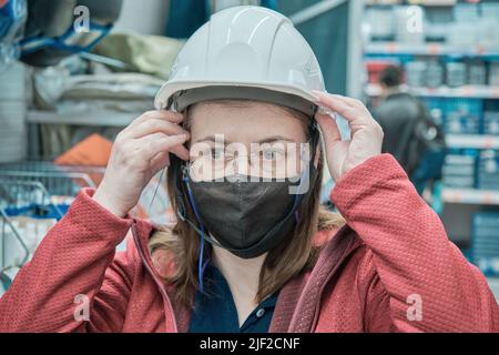 Donna in un negozio di materiali da costruzione misura su un casco di sicurezza bianco. Primo piano Foto Stock