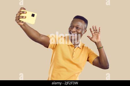 Felice uomo africano che sventola ciao come prende selfie o fa videochiamata sul telefono cellulare Foto Stock