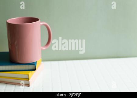Tazza rosa e taccuino su una scrivania bianca. Parete con sfondo verde kaki Foto Stock