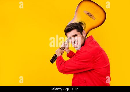 Ritratto di attraente ragazzo pazzo rude che tiene la chitarra combattendo isolato su sfondo di colore giallo brillante Foto Stock