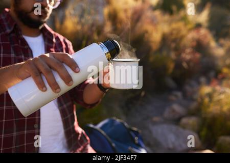 Un uomo versa l'acqua calda da una fiasca nella tazza di caffè mentre si accampava Foto Stock