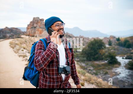 Un giovane zaino in spalla ride su una chiamata in montagna mentre si fa un'escursione in autunno Foto Stock