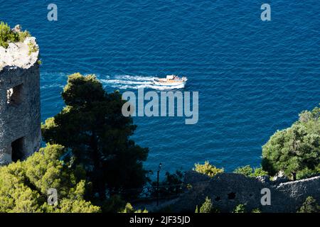 Vista dall'alto, vista mozzafiato di una barca gozzo con i turisti a bordo vela su un'acqua blu. Defocusò Torre dello Ziro in primo piano. Foto Stock