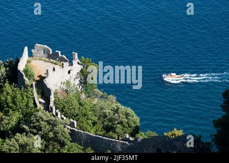 Vista dall'alto, vista mozzafiato di una barca gozzo con i turisti a bordo vela su un'acqua blu. Defocusò Torre dello Ziro in primo piano. Foto Stock