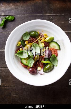 Insalata semplice con olive verdi e Kalamata, cetrioli, ciliegi e pomodori marinati, capperi e peperoni Jalapeno. Sfondo di legno marrone. Vista dall'alto. Foto Stock