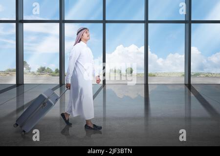 Uomo arabo che indossa keffiyeh camminando con una valigia per viaggiare Foto Stock