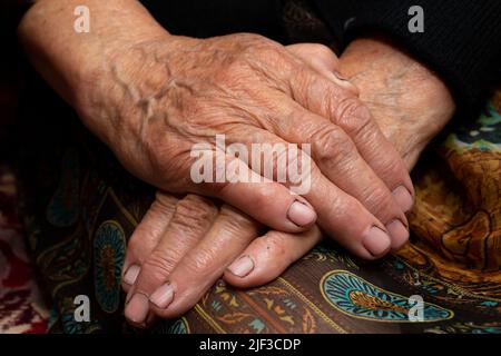 Nonna seduta con le mani in grembo, su sfondo scuro Foto Stock