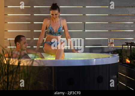 Coppia caucasica nel loro 40s godendo il loro tempo libero in una vasca idromassaggio Garden Spa durante la calda serata estiva. Tema relax e benessere. Foto Stock