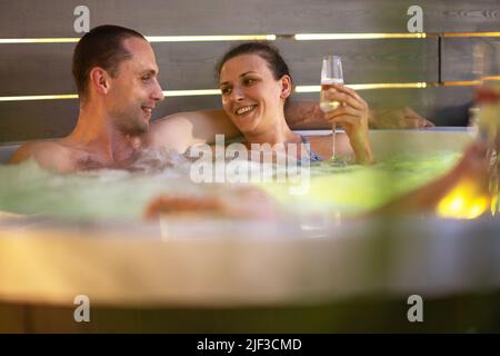 Coppia caucasica nel loro 40s che hanno tempo romantico nel loro giardino idromassaggio Spa vasca durante la calda sera d'estate. Tema ricreativo e benessere. Foto Stock