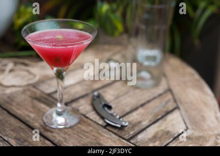 cocktail rosso con ghiaccio in vetro con gambo su superficie di legno Foto Stock