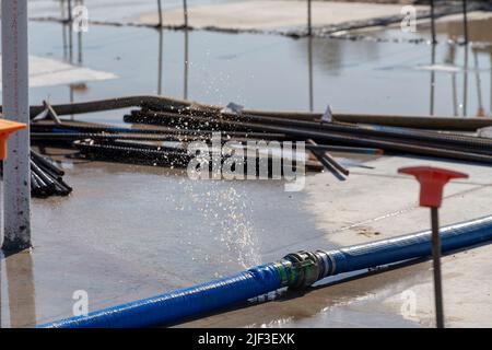 un tubo flessibile di acqua che perde su un cantiere da una pompa per svuotare una grande pozzanghera dopo un pesante rainstorm. waterpump firehose Foto Stock