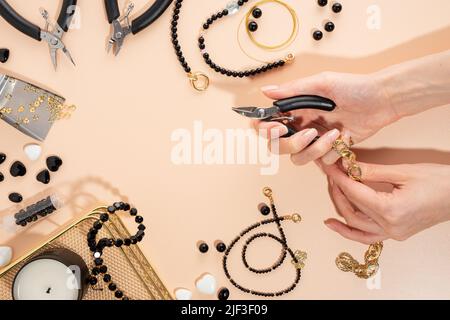 Utensili e accessori per gioielli fai-da-te sul posto di lavoro. Mano femmina con tagliafili. Piatto su sfondo beige. Composizione concettuale, vista dall'alto. Foto Stock