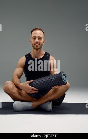 Man Foam Rolling. L'atleta si allunga utilizzando un rullo in schiuma. Foto Stock
