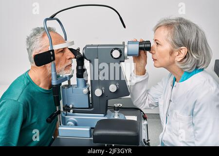 Optometristo che fa il test della vista per l'uomo anziano alla clinica moderna di oftalmologia. Esame visivo e diagnostica visiva Foto Stock