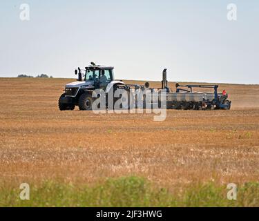 EMPORIA, KANSAS - 28 GIUGNO 2022 Farmer che guida il suo trattore con seminatrice automatica dietro le unità avanti e indietro sopra campo di grano recentemente raccolto piantando semi per una raccolta invernale di grano rosso Foto Stock