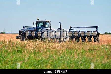 EMPORIA, KANSAS - 28 GIUGNO 2022 Farmer che guida il suo trattore con seminatrice automatica dietro le unità avanti e indietro sopra campo di grano recentemente raccolto piantando semi per una raccolta invernale di grano rosso Foto Stock