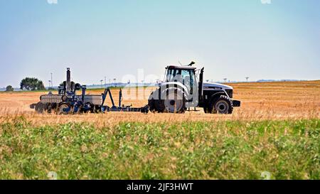 EMPORIA, KANSAS - 28 GIUGNO 2022 Farmer che guida il suo trattore con seminatrice automatica dietro le unità avanti e indietro sopra campo di grano recentemente raccolto piantando semi per una raccolta invernale di grano rosso Foto Stock