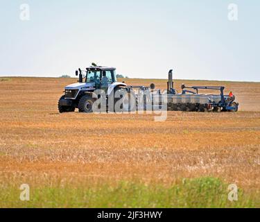 EMPORIA, KANSAS - 28 GIUGNO 2022 Farmer che guida il suo trattore con seminatrice automatica dietro le unità avanti e indietro sopra campo di grano recentemente raccolto piantando semi per una raccolta invernale di grano rosso Foto Stock