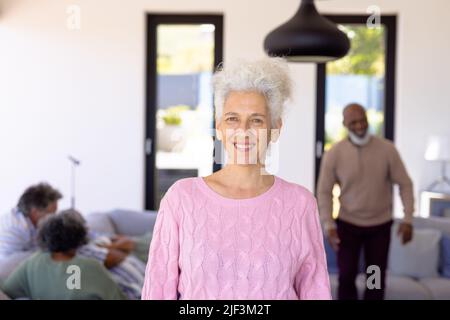 Ritratto di sorridente caucasica anziana in piedi con amici multirazziali in background Foto Stock