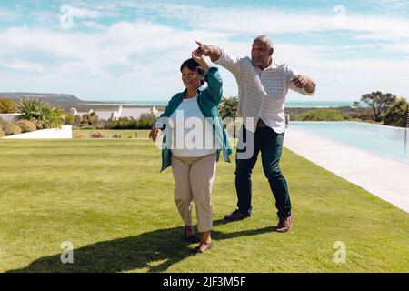 Felice biraciale uomo anziano ballando con donna su terra erbosa contro il cielo in cantiere in estate Foto Stock