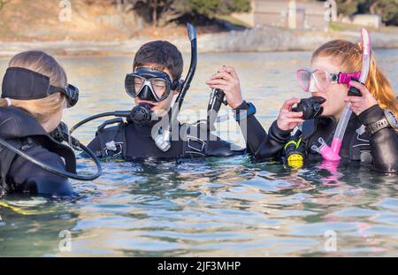 I subacquei si allenano in mare guardando il loro istruttore che si prepara a immergersi con le loro maschere e le loro manichette deflatore sollevate Foto Stock