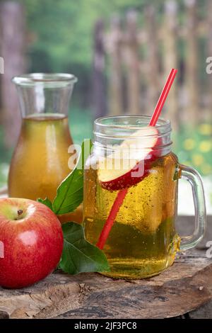 Bicchiere di succo di mela e mela rossa su vecchio blocco di legno con sfondo rurale Foto Stock