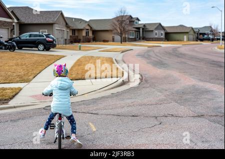 Ragazza che guida una bicicletta in modo sicuro attraverso la strada fino a un marciapiede indossando un casco. Foto Stock