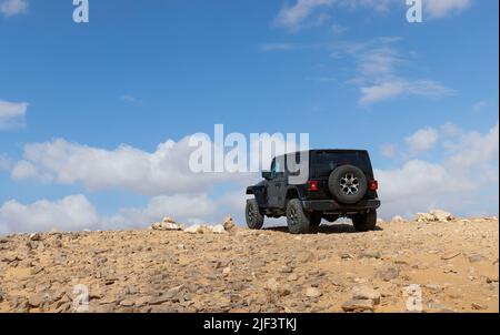 il veicolo fuoristrada attraversa il deserto contro un cielo blu con le nuvole Foto Stock