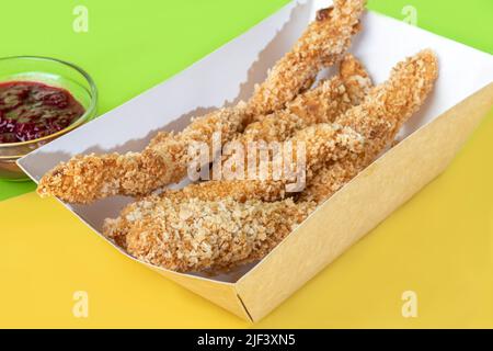 Strisce di pollo in pastella con salsa di ciliegia in un piatto di carta. Fast food. Sfondo colorato. Spazio di copia Foto Stock