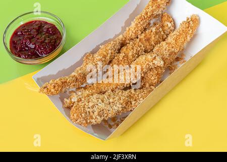 Strisce di pollo in pastella con salsa di ciliegia in un piatto di carta. Fast food. Sfondo colorato. Spazio di copia Foto Stock