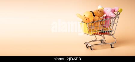 Mini carrello per lo shopping per bambini pieno di morbidi giocattoli per bambini sul banner con spazio per la copia del testo pubblicitario. Foto di alta qualità Foto Stock