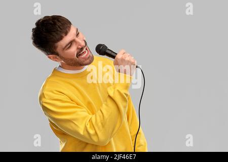 uomo in felpa gialla con microfono che canta Foto Stock