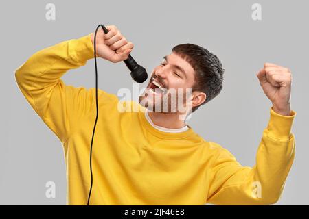 uomo in felpa gialla con microfono che canta Foto Stock