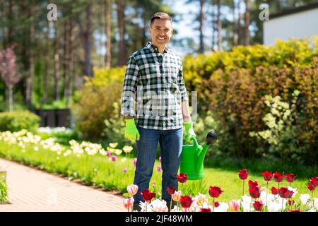 uomo felice con annaffiatoio e fiori in giardino Foto Stock