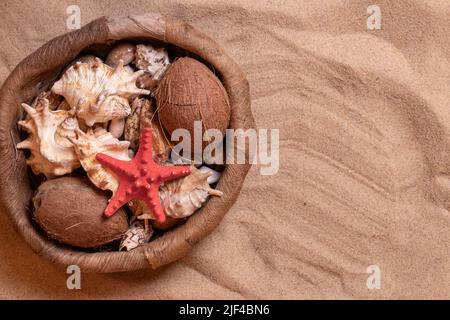 Conchiglie in un cestino di vimini sulla sabbia. Vacanze estive su sfondo marino con spazio per il testo. Vista dall'alto. Foto Stock