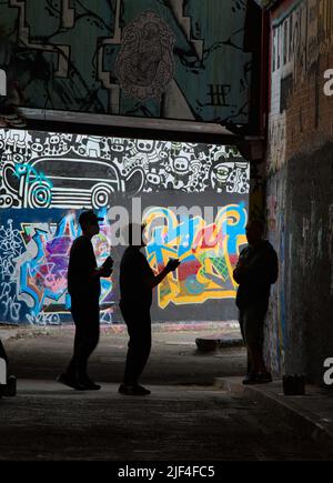 Silhouette di Graffiti Artisti con lattine spray sotto un ponte in Un tunnel vicino Waterloo Station, Londra Regno Unito Foto Stock