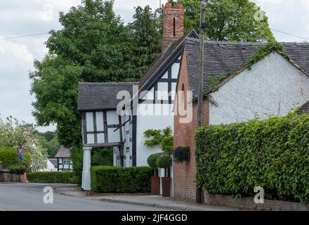 Vista laterale di una strada che guarda un'antica casa bianca e nera nella campagna del Cheshire con alberi verdi e siepi Foto Stock