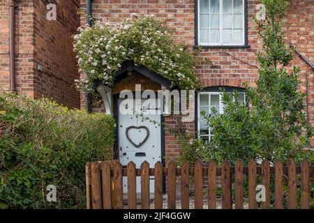 Cottage con piccole rose rosa che crescono sopra la porta chiamato cottage rosa con una porta bianca anteriore Foto Stock