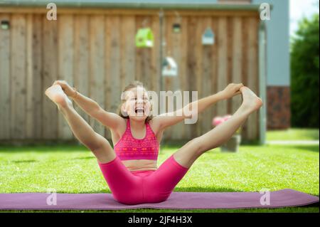 Ragazza felice sportiva adolescente che pratica pilates su tappeto yoga su erba a cortile Foto Stock