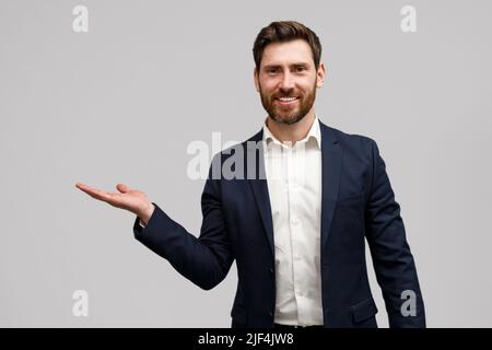 Un uomo d'affari sorridente guarda alla macchina fotografica e punta su qualcosa con le mani a fianco Foto Stock