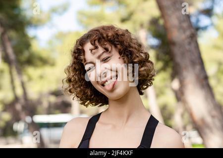 Cute donna caucasica che indossa il reggiseno sportivo in piedi sul parco cittadino, esterno che attacca lingua felice con espressione divertente. Concetto di emozione. Foto Stock