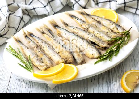 Primo piano di capelin fritto su un piatto di porcellana bianca con limone, rosmarino e spezie. Concetto di cibo sano. Messa a fuoco selettiva. Foto Stock