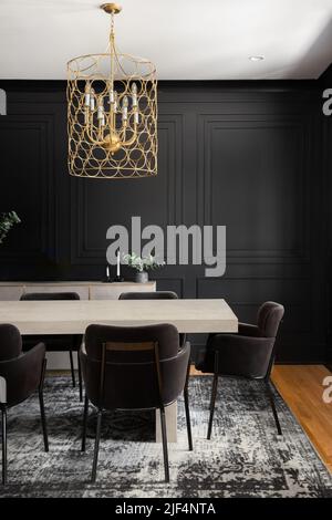 Un'accogliente sala da pranzo con un lampadario d'oro sopra un tavolo di legno e pareti in legno. Foto Stock
