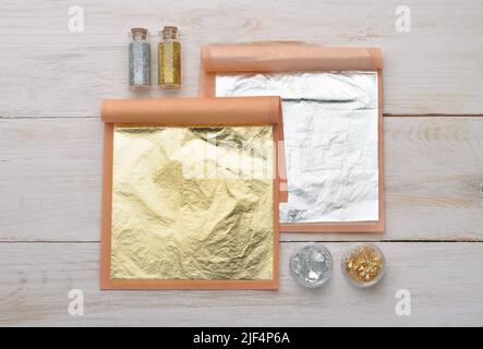 Vista dall'alto di fogli in oro e argento, scaglie e polvere di cibo naturale commestibile su tavola di legno bianco Foto Stock