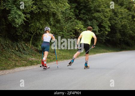 Atletica donna e uomo allenarsi insieme sul roller ski. Vista posteriore. Spazio di copia. Concetto di competizione, biathlon e allenamento estivo. Foto Stock